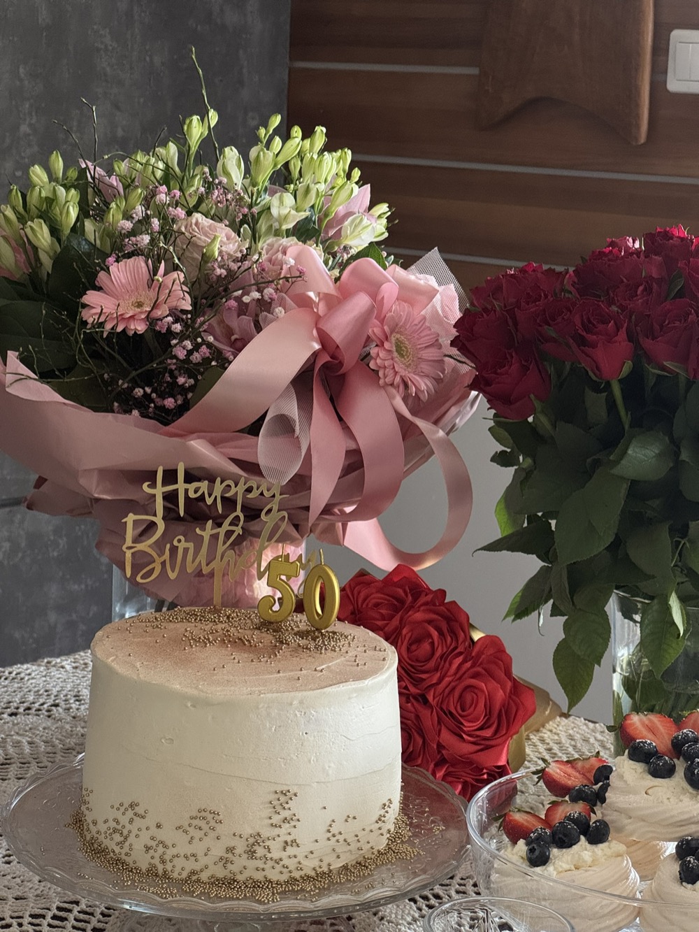 Tort na 50. urodziny ze złotym brokatem u podstawy i toperem Happy Birthday 50, otoczony bukietami róż